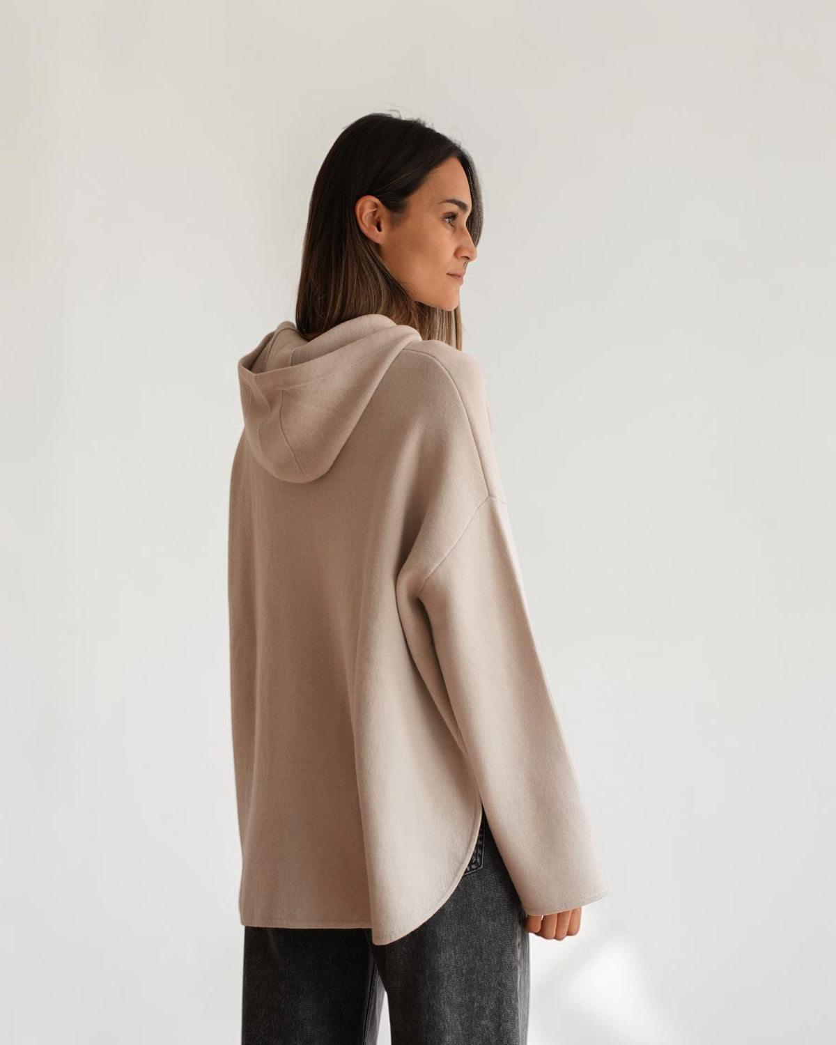 Hellgraue Kapuzen-Strickjacke am Model, schräge Rückansicht mit Kapuze und gerundetem Saum.