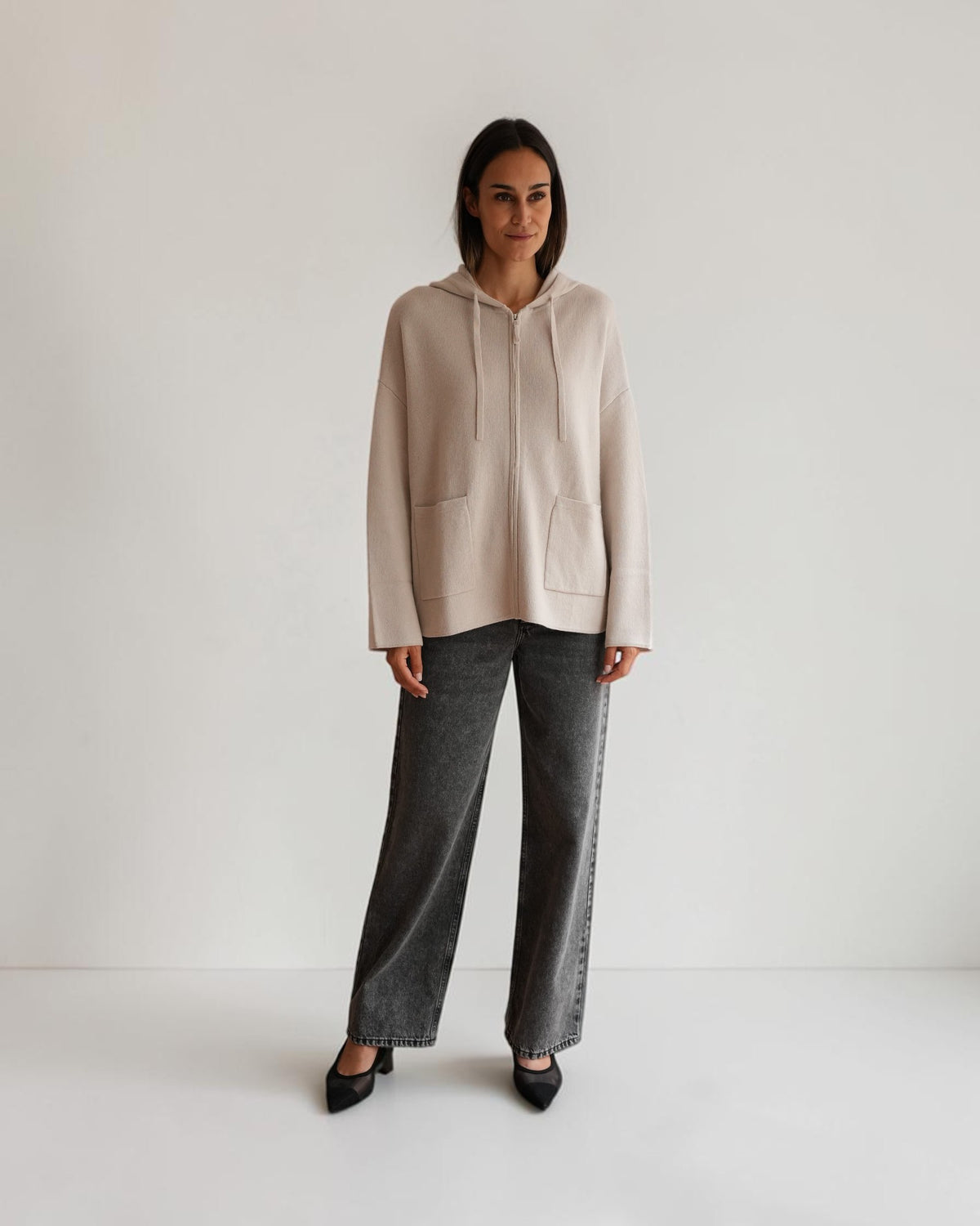 Hellgraue Oversized-Strickjacke mit Reißverschluss am Model, Vorderansicht mit heruntergelassener Kapuze.