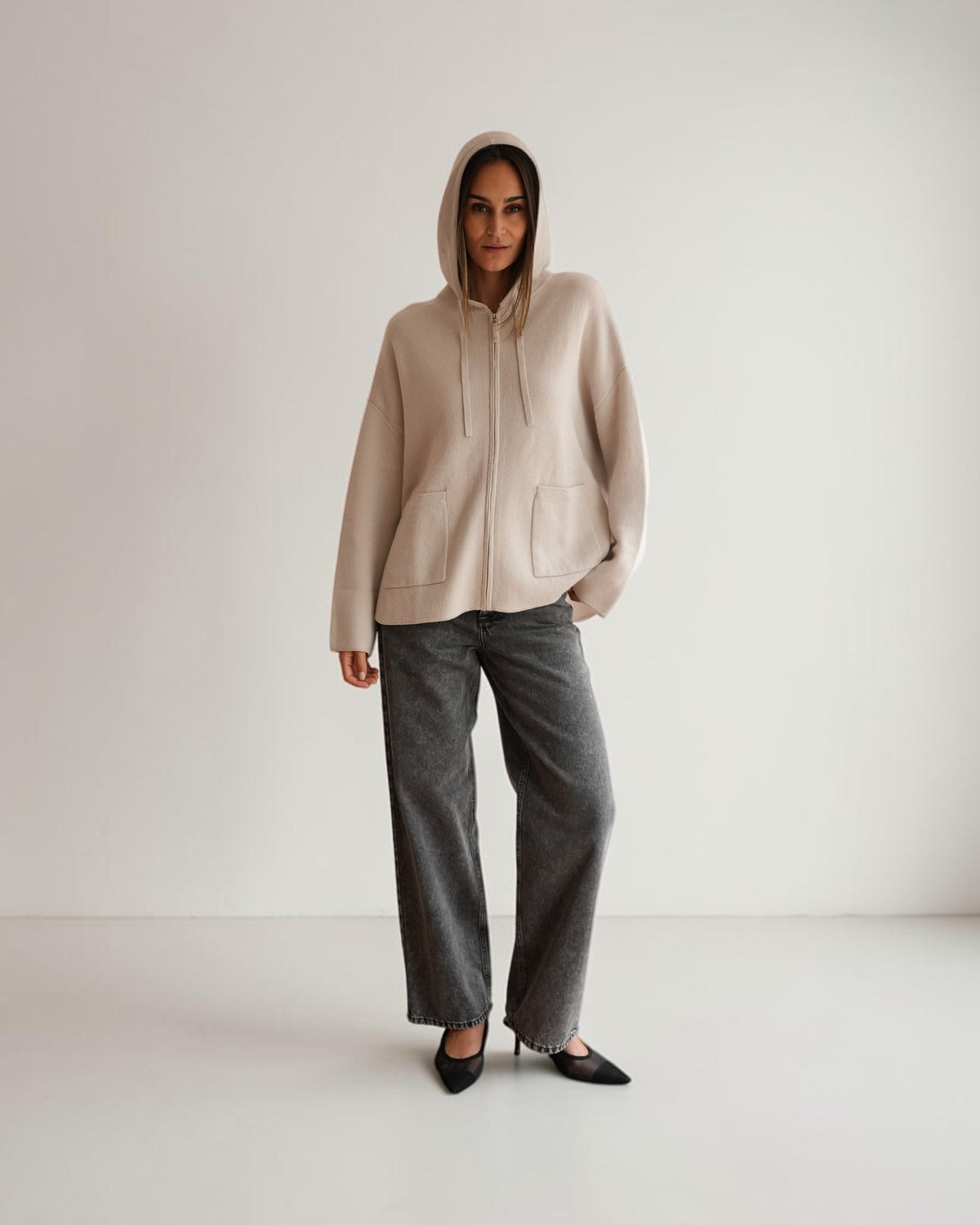Hellgraue Oversized-Strickjacke mit Reißverschluss am Model, Vorderansicht mit aufgesetzter Kapuze.