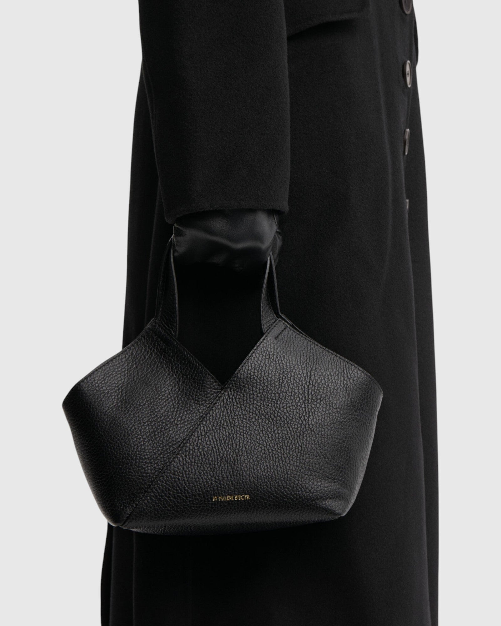 By Malene Birger kleine schwarze Ledertasche mit breiten Henkeln seitlich am Model getragen