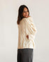 Cream cable-knit sweater with openwork panels, rear three-quarter view on model.