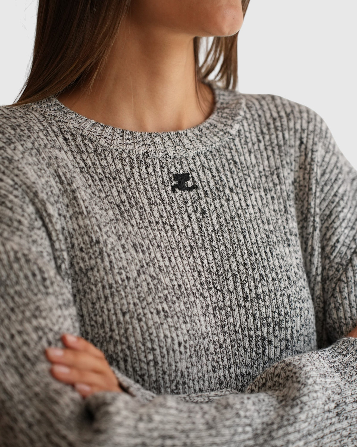 Close-up of the black and white melange Courrèges sweater with a crew neckline and black logo embroidery