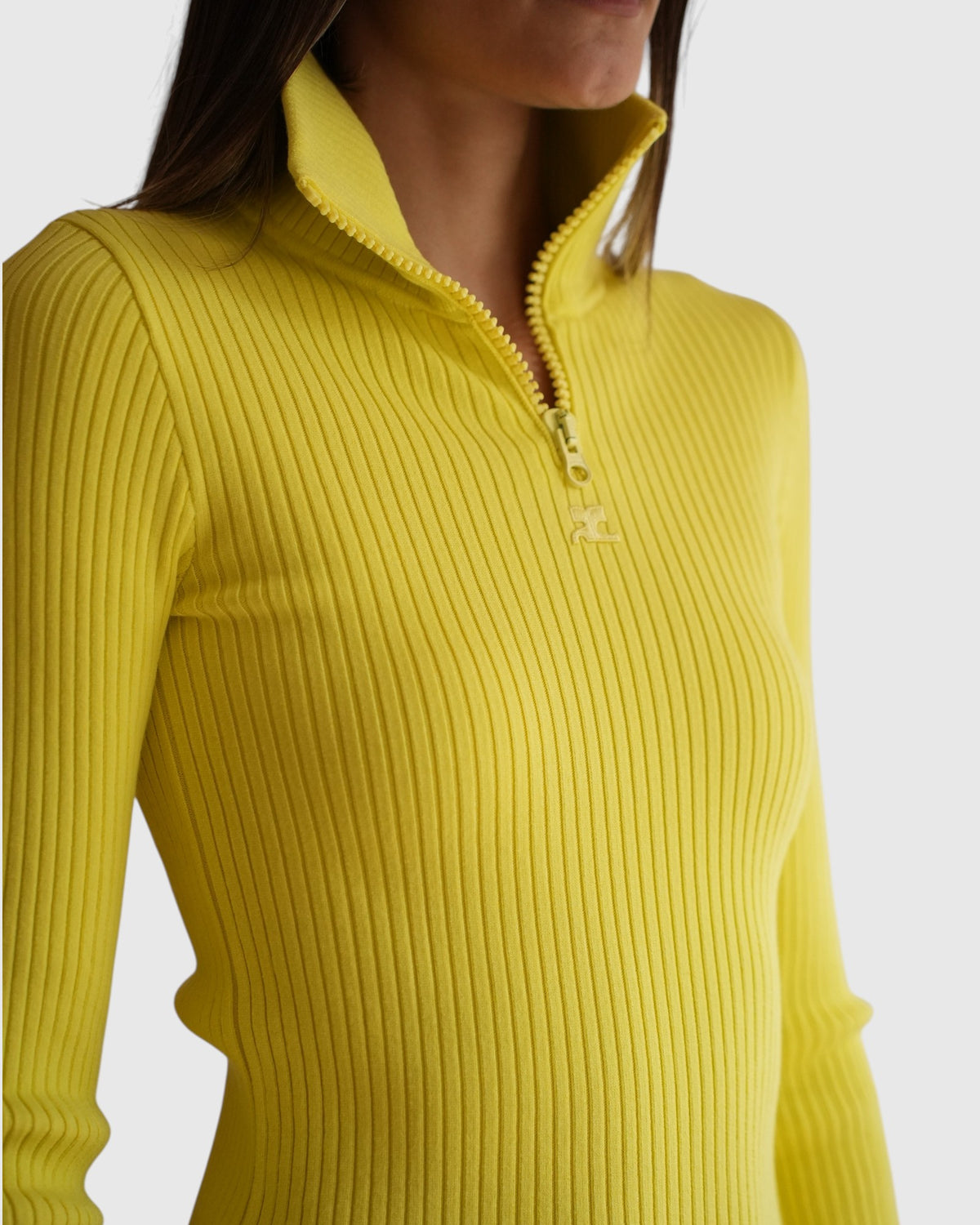 Detail des gelben Rippstrick-Pullovers mit teilweise geöffnetem Zip-Kragen und tonalem AC-Logo.