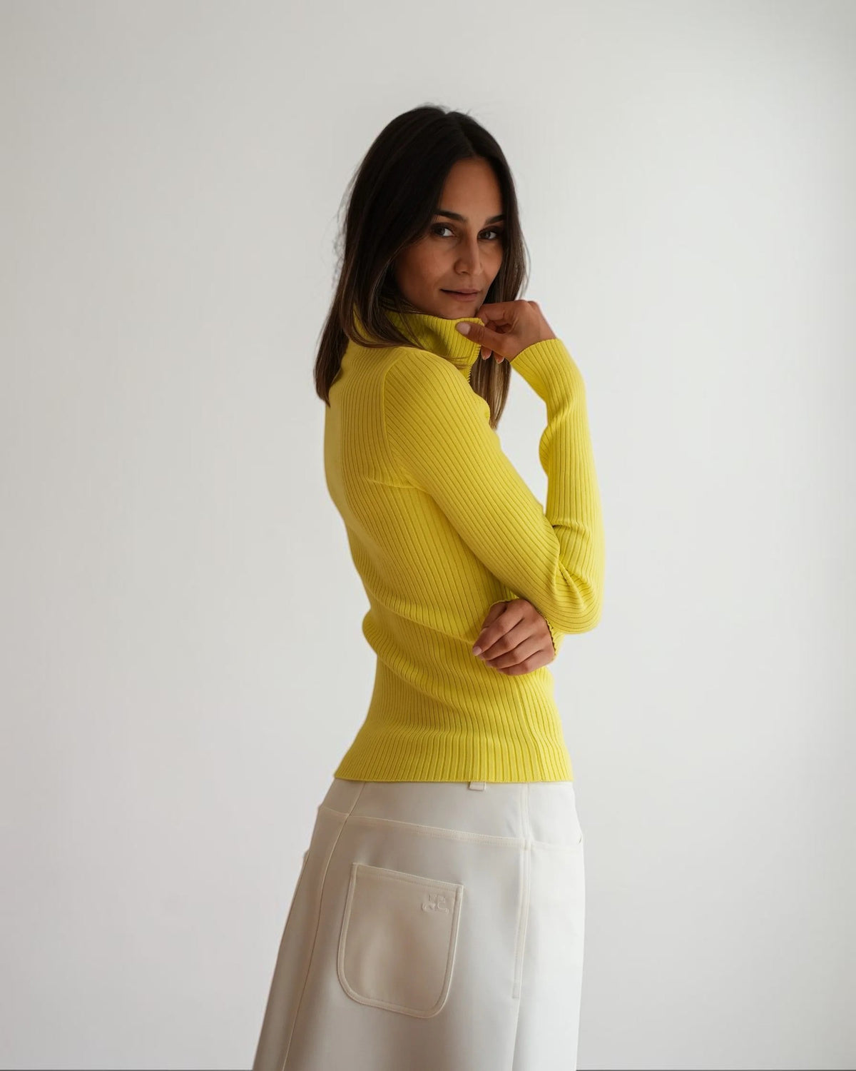 Gelber Rippstrick-Pullover mit hohem Kragen und körpernaher Passform, seitlich am Model getragen.