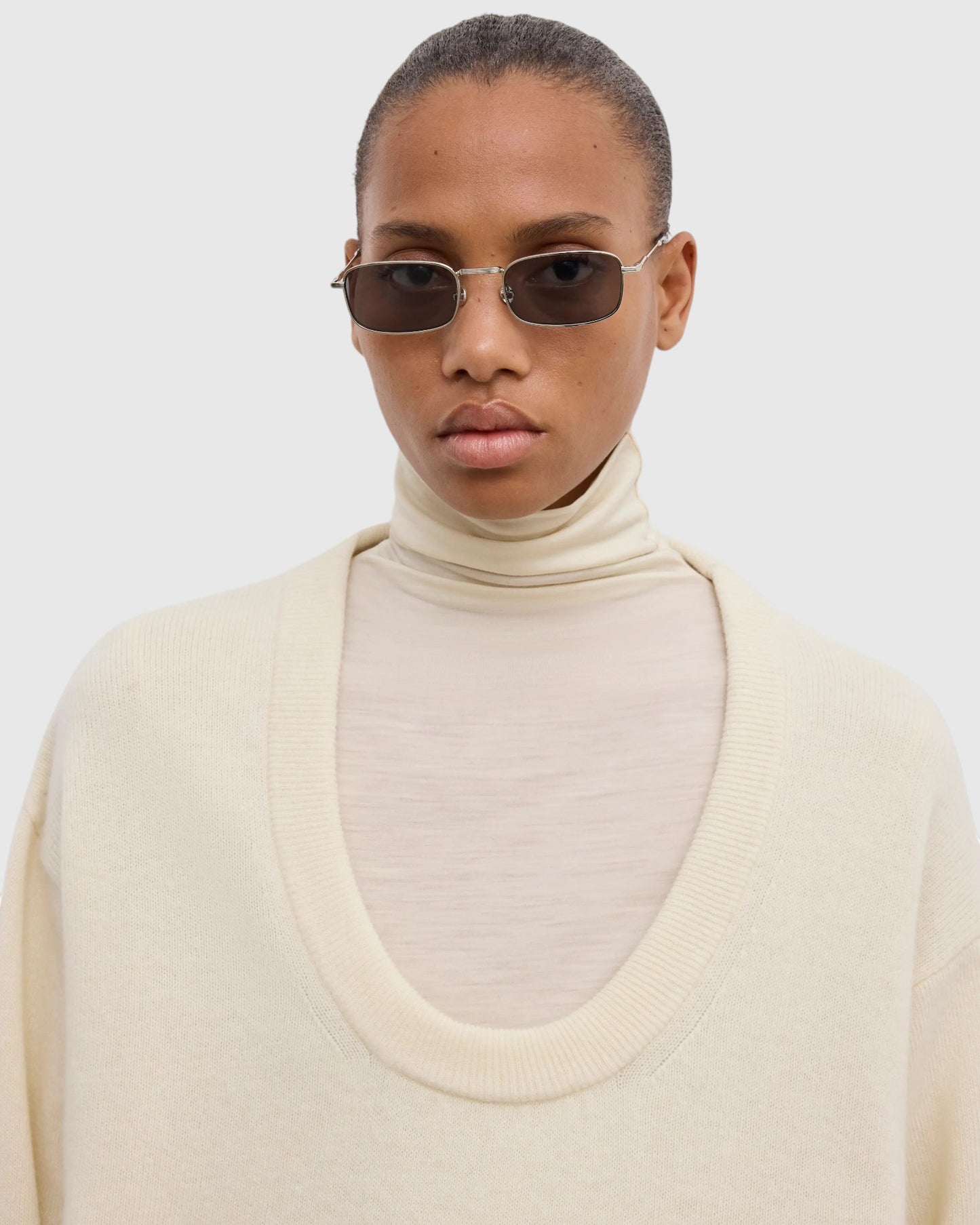 Detail des tiefen Rundhalsausschnitts am cremeweißen Wollpullover