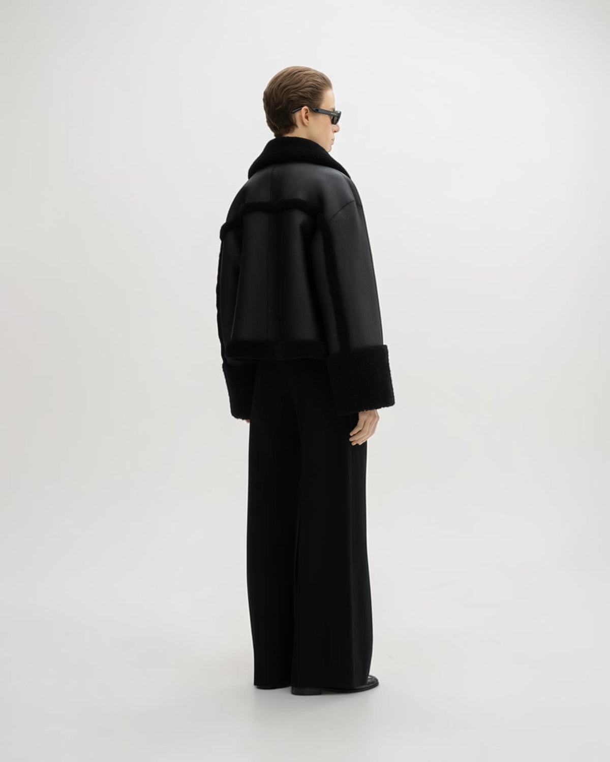 House of Dagmar schwarze Lammfelljacke am Model schräg von hinten mit Fellbesatz am Rücken und am Saum