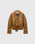 Saffron-brown cropped leather jacket with a waist belt, shirt collar and buckled cuffs, front view.