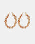 Oval gold-tone hoop earrings with pink and terracotta stones and winding metal details, shown as a pair.