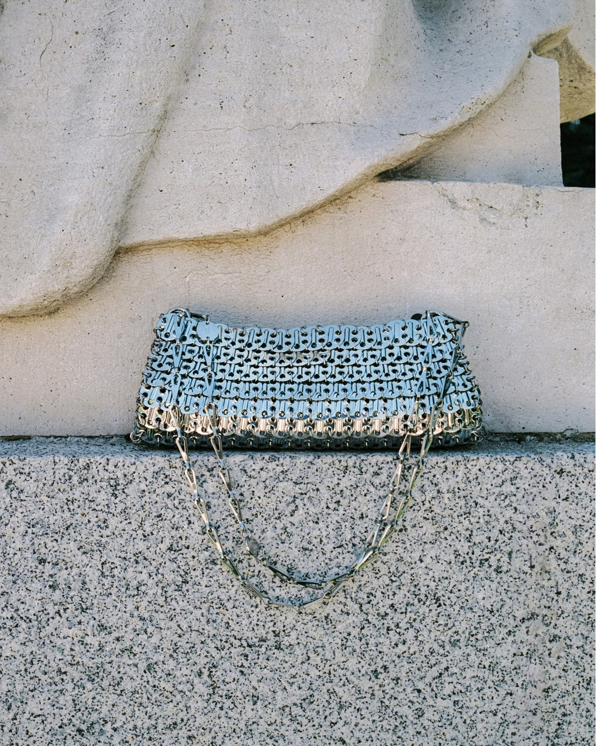 Rabanne 1969 Clutch in Silber mit herabhängendem Kettenriemen auf einer steinernen Stufe