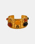 Wide gold cuff bracelet with yellow, red, black and brown cabochons and gold bead details, front view.