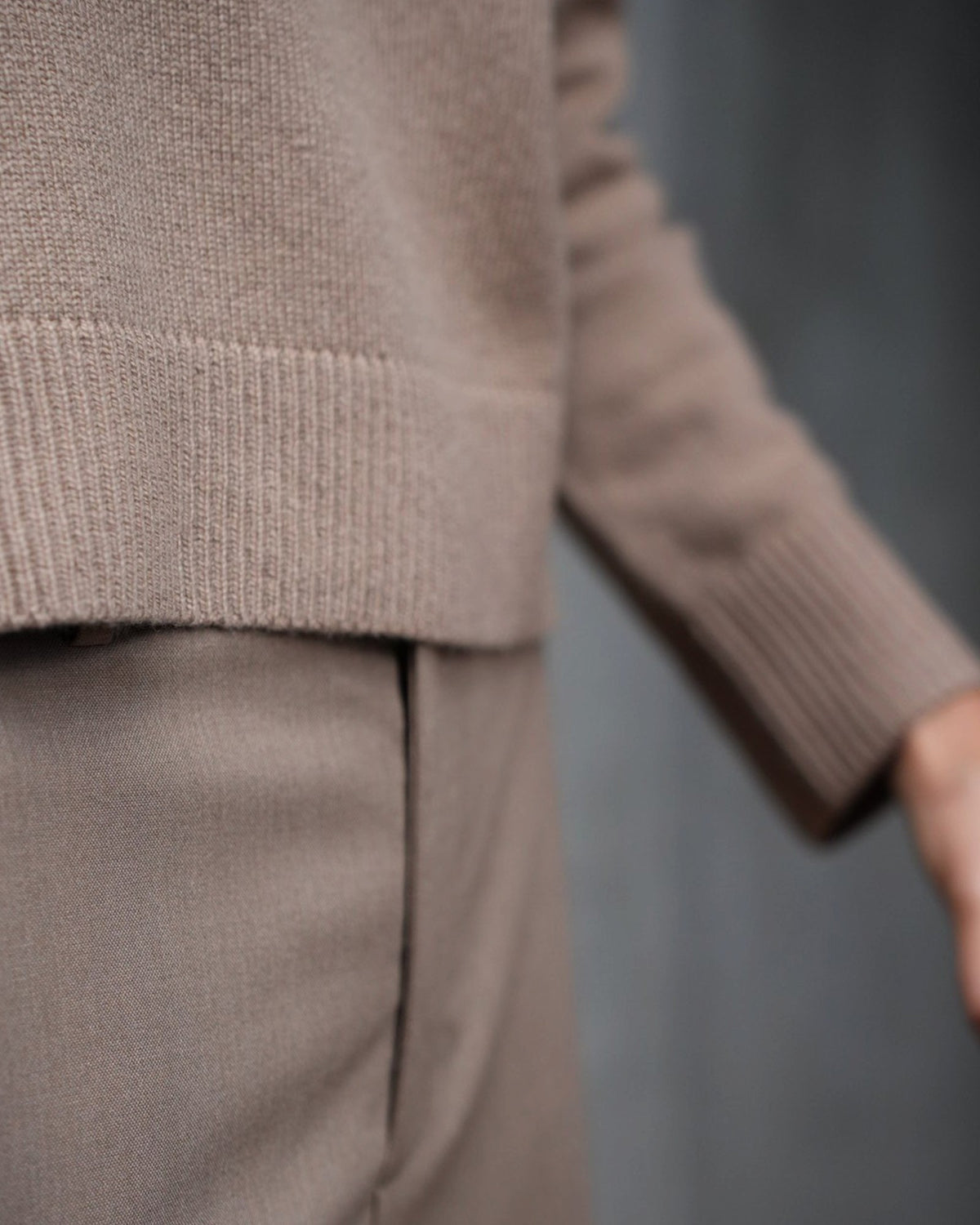 Dunkelbeige Hose von Vince unter einem camelfarbenen Strickpullover am Model, Ausschnitt mit Fokus auf den Stricksaum.