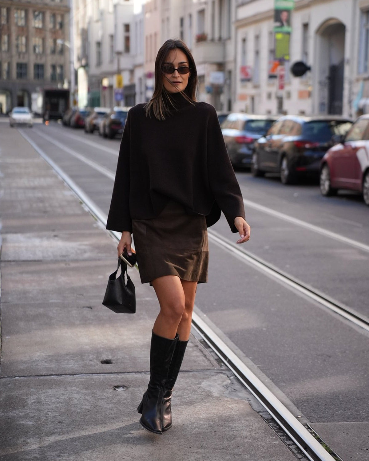 Model mit braunem Velourslederrock von Vince und hohen schwarzen Stiefeln, Ganzkörperansicht.